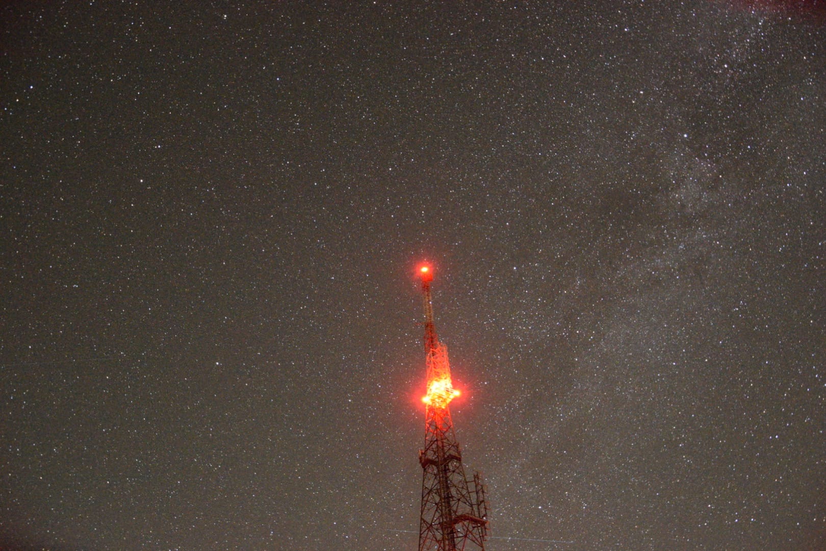 A mobile signal tower blinking red light with stars in the background
