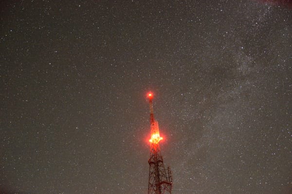 A mobile signal tower blinking red light with stars in the background